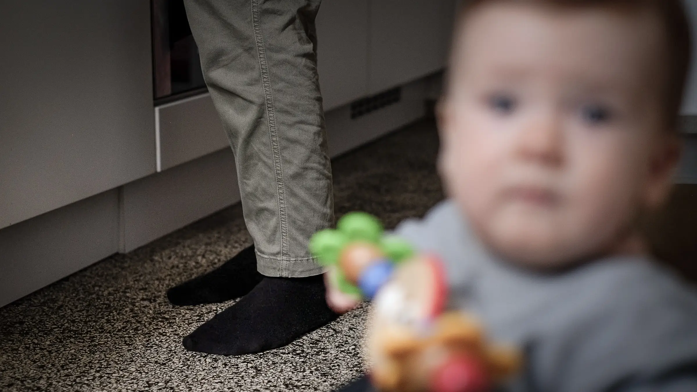 Kind, verschwommen, sitzt in der Wippe, erwachsene Person im Hintergrund